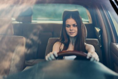 Araba süren genç bir kadın odaklanmış bir ifade ve uzun koyu renk saçlar sergiliyor. Gündelik kıyafetler giyiyor, modern bir araba ile özgürlük ve bağımsızlığı simgeliyor..