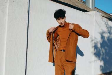 Moda ileri görüşlü bir erkek, parlak beyaz bir arka plana karşı modern şehir tarzını sergileyen kahverengi bir elbise içinde güven içinde poz verir.