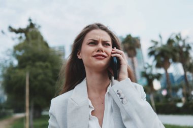 Beyaz ceketli genç beyaz kadın telefonda konuşurken stresli ve endişeli duygular sergiliyor. Finansal krizi veya şehir yeşilliği geçmişi olan iş sorunlarını sembolize ediyor..