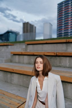 Çağdaş bir şehir manzarasına karşı kurulan şık bir iş kıyafetine güvenen bir kadın. Görüntü, profesyonel hırsı ve modayı sofistike bir şekilde ön plana çıkarıyor..