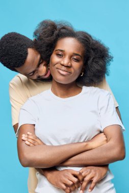 Neşeli bir çift Afrika kökenli parlak mavi arka plan karşısında samimi bir anı paylaşıyor, günlük kıyafetler giyiyor, aşkı ve bağlantıyı simgeliyor.