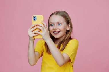 Sarı gömlekli heyecanlı kız pembe arka planda selfie çekiyor, mutluluk ve neşeyi yansıtıyor, sosyal medya ve yaşam tarzı teması için mükemmel.