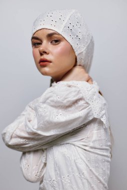 Açık tenli, beyaz bir elbise ve başörtüsü takan genç bir kadın model, zarafet ve zarafeti vurgulayan yumuşak odaklı, minimalist bir şekilde sükunet ve güzellik yayar.