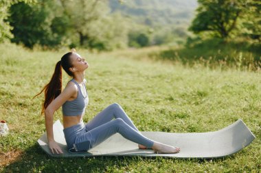Serin, genç bir kadın dışarıda yoga yapıyor, yemyeşil manzaranın ortasında sükuneti ve farkındalığı somutlaştırıyor. Bu güzel ifadesini tamamlayan şık bir aktivite kıyafeti giyiyor.