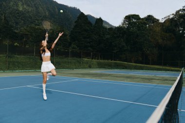 Genç ve dinamik bir bayan atlet mavi bir tenis kortunda, yemyeşil bir zemine karşı odak ve enerji gösterisi yapıyor, sporla ilgili görseller için mükemmel.