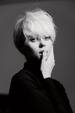 Kısa, kıvırcık sarı saçlı, siyah balıkçı yakalı, dalgın bir ruh hali içinde genç bir kadın. Yumuşak ışık dramatik bir atmosfer yaratır..