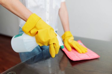 Sarı eldivenli bir kadın cam masayı temizliyor. Profesyonel olarak bir cam yüzeyini dikkatlice ve detaylara dikkat ederek temizliyorum. parlak ve temiz çalışma alanı kavramı.