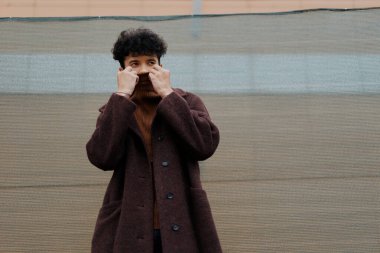 Kahverengi paltolu moda adamı yeşil duvarın önünde el ele tutuşuyor..