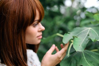 Kızıl saçlı bir kadın bahçedeki yemyeşil yapraklara hayran.