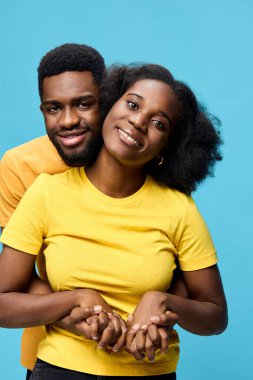 Birbirlerine uyumlu sarı t-shirtler giyen neşeli bir Afrikalı çift, parlak mavi bir arka plana karşı dururlar. Aşkı ve birlikteliği sembolize ederler. Gülüşleri mutluluğu ve bağlantıyı ifade eder.