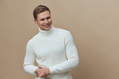 Beyaz örgü balıkçı yaka kazak giyen gülümseyen beyaz adam bej arka planda gevşemiş mutlu bir yüz arıyor. Sonbahar konforu ve gündelik sıcaklıkla dijital detoks kavramı