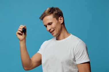 Elinde akıllı saat tutan gülümseyen adam beyaz tişört giyen giyilebilir fitness izleyicisi mavi arka plan teknolojisi aletine bakıyor dijital cihaz siber güvenlik konsepti içeriyor