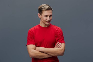 Kırmızı tişörtlü genç adam gri arka planda izole edilmiş düşünceli bir ifadeyle aşağıya bakıyor. Günlük kıyafet, kısa saç, stüdyo portresi ruh sağlığı ve aletler konsepti