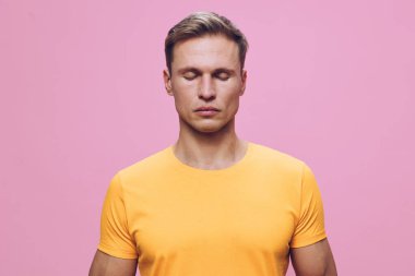 Sakin bir adam, pembe arka planda duran sarı tişört giyerek meditasyon yapıyor, farkındalık ve zihinsel sağlığa odaklanıyor, refahı ve rahatlığı teşvik ediyor. Konsept: Ruh sağlığı ve