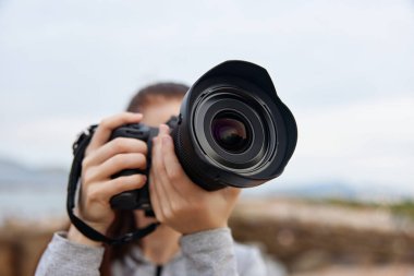 Kadın bir fotoğrafçı kamerayı tutkulu bir şekilde açık havada doğal bir arkaplana tutarak, fotoğrafçılığa olan sevgisini canlı sıcak renklerle ve sanatıyla duygusal bir bağlantıyla vurguluyor.