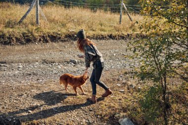 Güneşli bir günde, sakin bir kırsal yolda köpeğini gezdiren bir kadın.