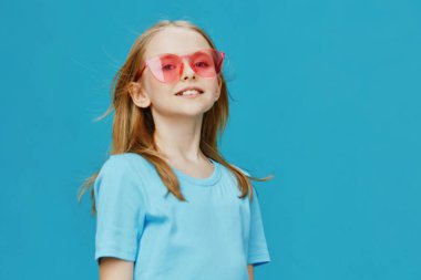 Pembe güneş gözlüklü ve mavi gömlekli genç bir kızın parlak ve neşeli görüntüsü, turkuaz bir arkaplan üzerine kurulmuş bu neşeli sahne yaz eğlencesinin, iyimserliğinin ve masumiyetin özünü yakalıyor.