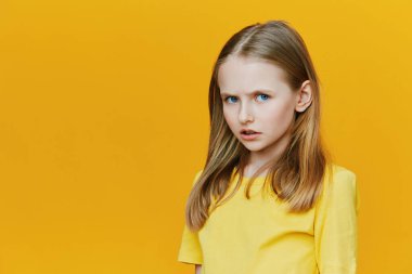 Uzun sarı saçlı, parlak sarı gömlekli genç bir kız canlı sarı bir arka plana karşı düşünceli bir yüz ifadesi sergiliyor. Ruh halini ve renk farkını vurguluyor.