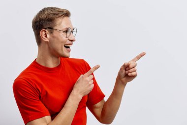 Kırmızı tişört giyen ve yuvarlak gözlükler takan gülümseyen bir adam. Yan tarafa bakıyor ve işaret ediyor. Sıradan poz veriyor.