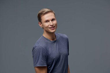 Kısa saçlı gülümseyen adam günlük kıyafet giymiş koyu gri arka planda duran kameraya bak. Genç beyaz adam pozitifliğini ve güvenini ifade ediyor. Kavram: gündelik tarzda dijital göçebe yaşam tarzı ve