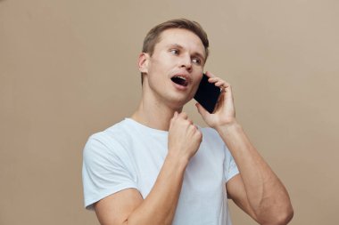 Beyaz tişörtlü, ağzı açık, beyaz tişörtlü, cep telefonuyla konuşan genç beyaz bir adam farklı zaman dilimlerinde dijital göçebe konseptiyle iletişim kuruyor.