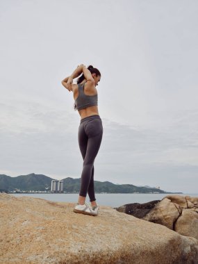 Gün doğumunda kumsalda gerinen gri spor giysili kararlı genç kadın kıyı geçmişi spor ve sağlıklı bir yaşam tarzını ön plana çıkarıyor.