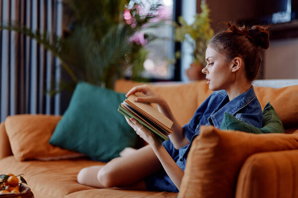 Relaxing woman on orange couch reading book and holding coffee cup in cozy living room