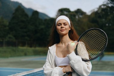 Spor kıyafeti ve saç bandı takmış kendine güvenen genç bayan tenisçi, sahada gülümsüyor, fevkalade bir doğası var, sportmenlik ve zindelik timsali
