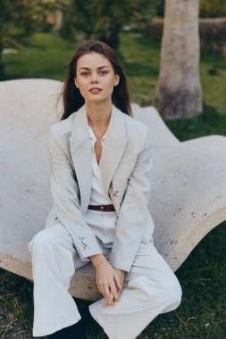 Bu profesyonel kadın, modaya uygun bir görünümü doğayla harmanlayarak şık iş kıyafetine güveniyor. Yumuşak renkler ve rahat duruş onun yaklaşımını ve profesyonelliğini vurguluyor..