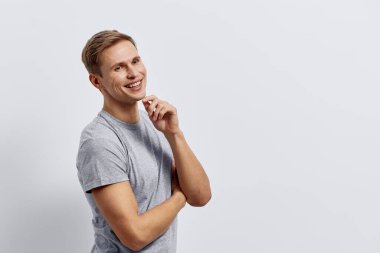 Gündelik gri tişörtlü gülümseyen beyaz adam kollarını kavuşturmuş açık gri arka plana karşı düşünceli bir ifadeyle yan yana bakıyor. Uzaktan çalışan dijital göçebe kavramı