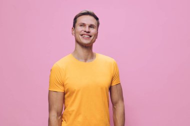 Kısa kahverengi saçlı, günlük sarı tişörtlü mutlu bir adam pembe bir zemine yaslanarak gülümsüyor, pozitifliğini, dostluğunu ve sıcaklığını ifade ediyor, yaşam tarzı için stüdyo fotoğrafı ve