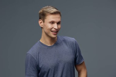 Stüdyo fotoğrafında gülümseyen, gri tişörtlü, güler yüzlü, esmer bir genç adam. Görüntü siber güvenlik ve dijital güvenlik temalarını yansıtıyor