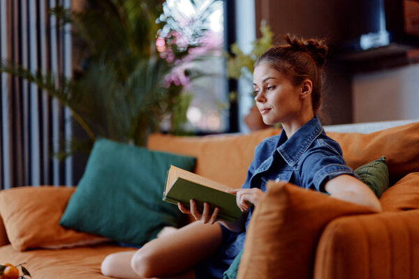 Woman sitting on orange couch reading book in cozy living room with soft natural light coming through window