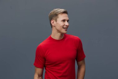 Kırmızı tişörtlü gülümseyen adam, gri arka planda izole edilmiş mutlu sıradan bir pozla yan tarafa bakıyor. Kafkasyalı genç adam dijital iletişimden zevk alıyor, yapay zekayla sohbet ediyor ve olumlu ifade veriyor.