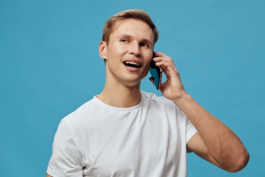 Mavi arka planda günlük beyaz tişörtle konuşan gülümseyen adam mutluluğu ve iletişimi ifade eden, dijital göçebe yaşam tarzını ve mobil teknoloji ile bağlanabilirliği temsil eden. Kavram