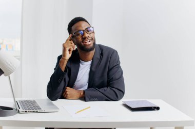 Resmi giyinmiş genç Afro-Amerikan iş adamı organize ofis masasında otururken telefonda dikkatle konuşuyor..