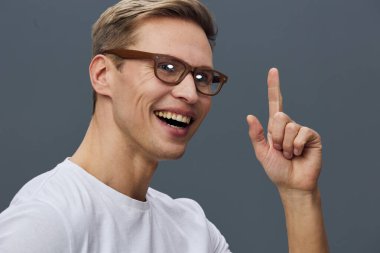 Gözlüklü, gülümseyen ve el hareketleriyle hareket eden mutlu genç adam, günlük kıyafet, gri arka plan, portre çekimi, pozitif titreşim, kişilik ve özgüven, stüdyo ayarları..