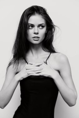 Siyah saçlı düşünceli genç bir kadın, basit siyah bir bluz giymiş, içgözlem duygularını aktarıyor. Minimalist biçim ve nötr arkaplan ifadesini vurguluyor.