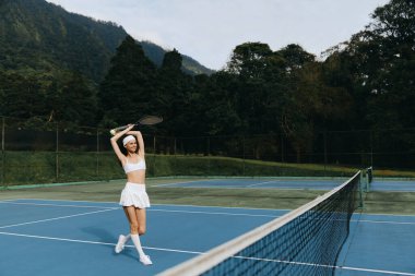 Dışarıda beyaz spor kıyafetleriyle tenisten hoşlanan enerjik genç bir kadın aktif bir yaşam tarzının özünü yakalıyor spor ve spor kavramları için mükemmel.