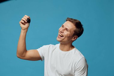 Beyaz tişört giyen, gülümseyen ve elinde arabanın anahtarlarını tutan mutlu beyaz bir adam mavi arka planda yalnızken heyecan ve özgürlük gösteriyordu. Pozitif duygu ve gelişigüzel olan dijital göçebe kavramı