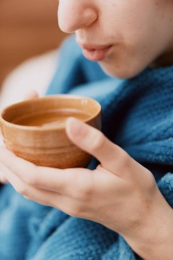 Mavi battaniyeli kadın elinde bir kase sıcak su ve çay tutuyor..
