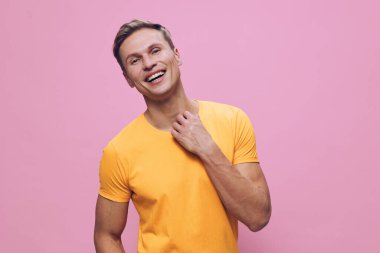 Sarı tişörtlü gülümseyen adam mutlu bir şekilde pembe arka planda poz veriyor, neşeli bir anı yakalıyor, gündelik moda, canlı renkler, pozitif ruh hali, stüdyo ortamı. Kavram: neşeli yaşam tarzı.