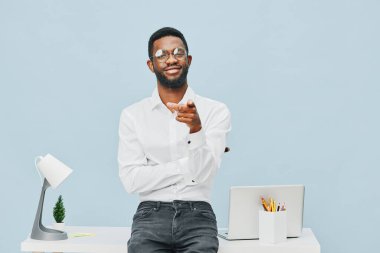 Günlük ofis kıyafeti giymiş, gözlüklü ve beyaz gömlekli neşeli, masa başında dizüstü bilgisayarı, masa lambası ve minimalist çalışma alanı ortamında saksıda duran kendine güvenen bir adam. Kavram