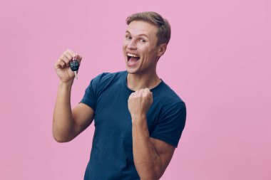 Sıradan mavi tişörtlü neşeli adam arabanın anahtarını tutuyor, heyecan ve mutluluk gösteriyor. Canlı pembe arka plan pozitif ruh hali, yaşam tarzı, başarı, başarı, kutlama, neşe vurguluyor.