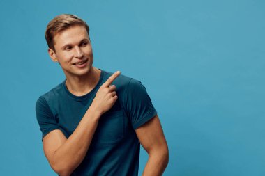 Mavi tişört giyen, gülümseyen, beyaz bir adam. Mavi tişört giyen ve parmak ucuyla işaret eden. Sade mavi arka planda tek başına duran. Olumlu duygular gösteren parlak bir ifade. Kavram