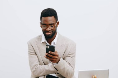 Gözlüklü profesyonel genç adam iş yerinde cep telefonuyla meşgul, günlük ceket giyiyor, beyaz bir arka plana karşı duruyor, teknoloji bilinci, iletişim becerileri, modern
