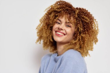 Şehvetli kıvırcık saçlı canlı bir genç kadın gülümserken mutluluk saçar. Tarafsız arka plan, neşeli ifadesini artırır. Bu da onu güzellik ve yaşam tarzı tasviri için ideal kılar.