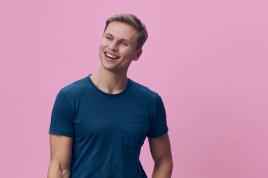 Mavi tişört giyen gülümseyen genç adam pembe arka planda izole edilmiş mutlu, kaygısız bir yaşam tarzına gülüyor ve uzaklara bakıyor canlı renklerle ve günlük tarzla dijital göçebe konsepti.