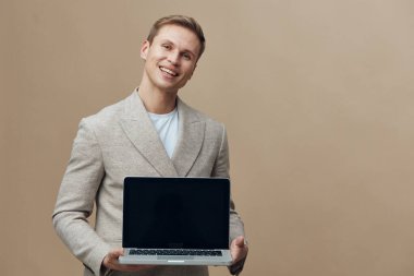 Gülümseyen mutlu beyaz adam dizüstü bilgisayarı elinde tutarken günlük ceket giyer bej arka plan dijital göçebe kavramına izole edilmiş online iletişim teknolojisi