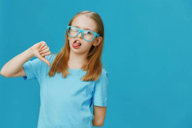 Mavi gözlüklü, mavi tişörtlü, neşeli ve çocukluk sevincini yansıtan komik bir ifade sergileyen genç bir kız.